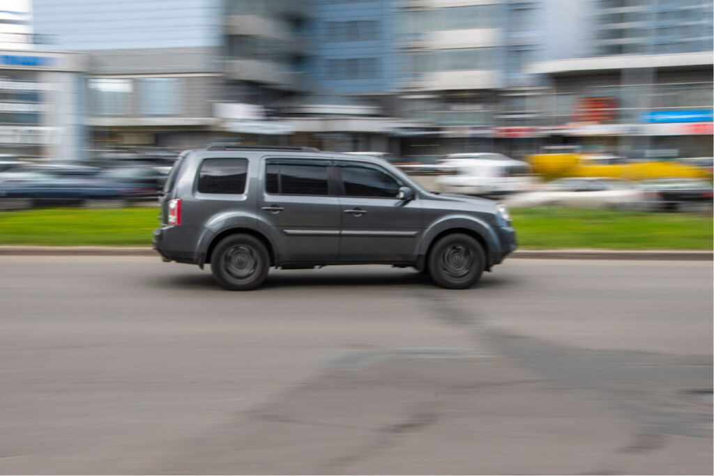 Grey Honda Pilot driving in city setting with blurred background